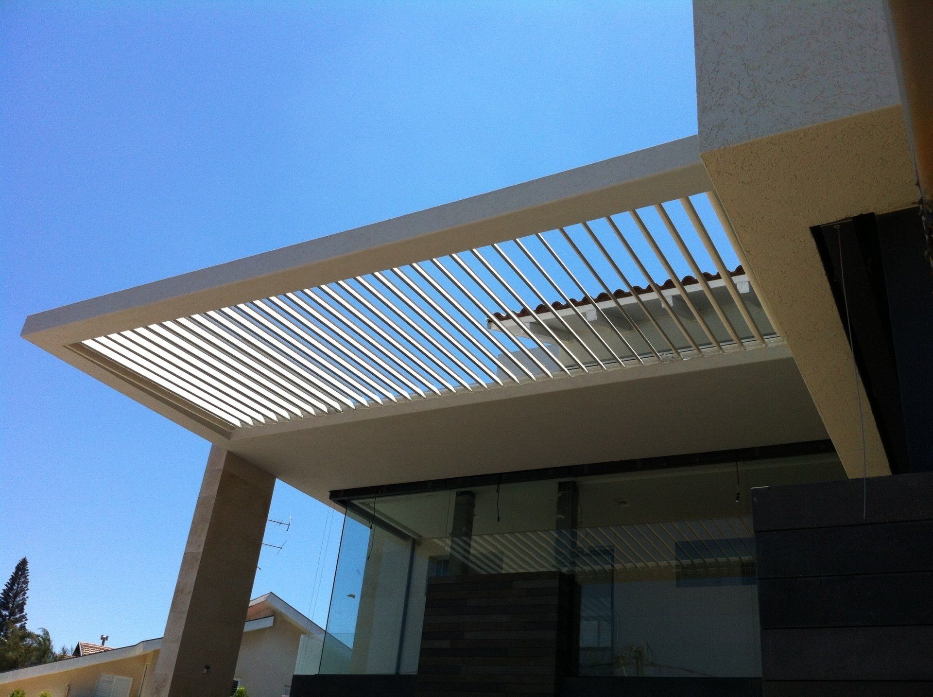 Modern house patio with a white slatted pergola against a clear blue sky
