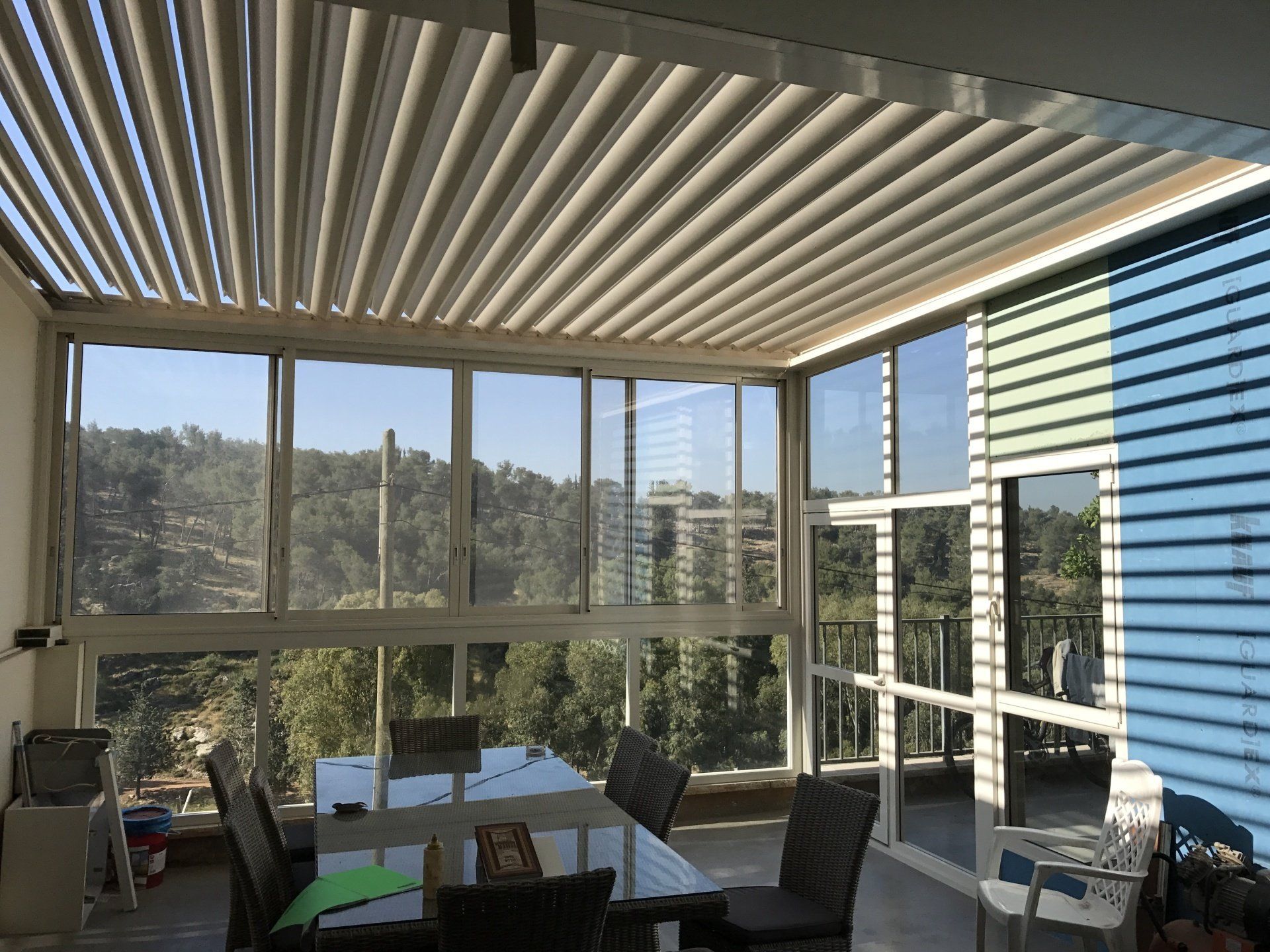 Modern patio with striped awning, glass walls, table, chairs, and hillside view