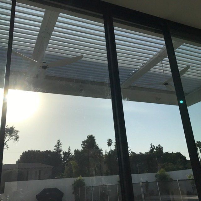 View through glass doors to a bright outdoor patio with a slatted roof and silhouetted trees at sunset