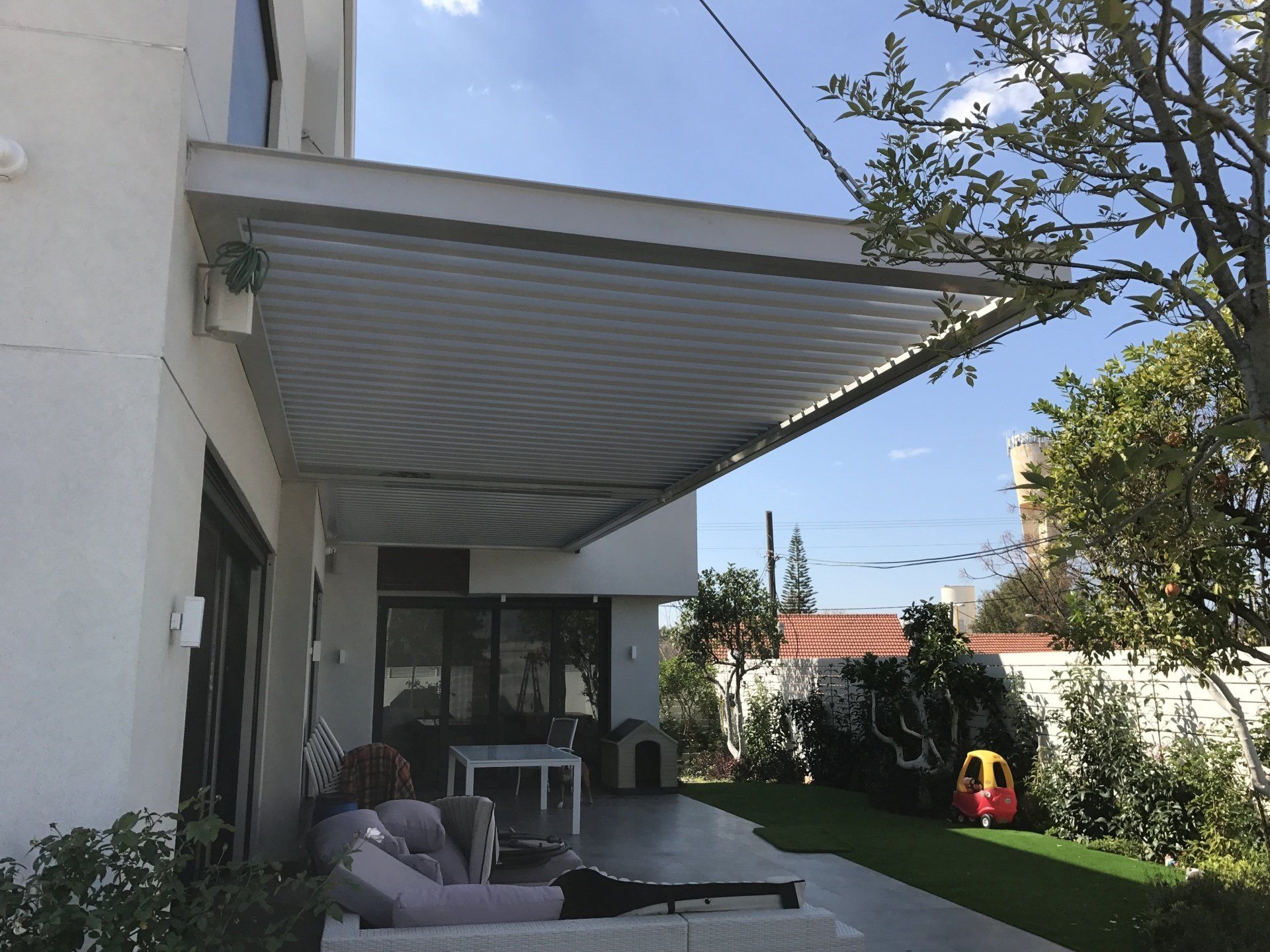 Patio with retractable awning, outdoor sofa, and garden view beside a house