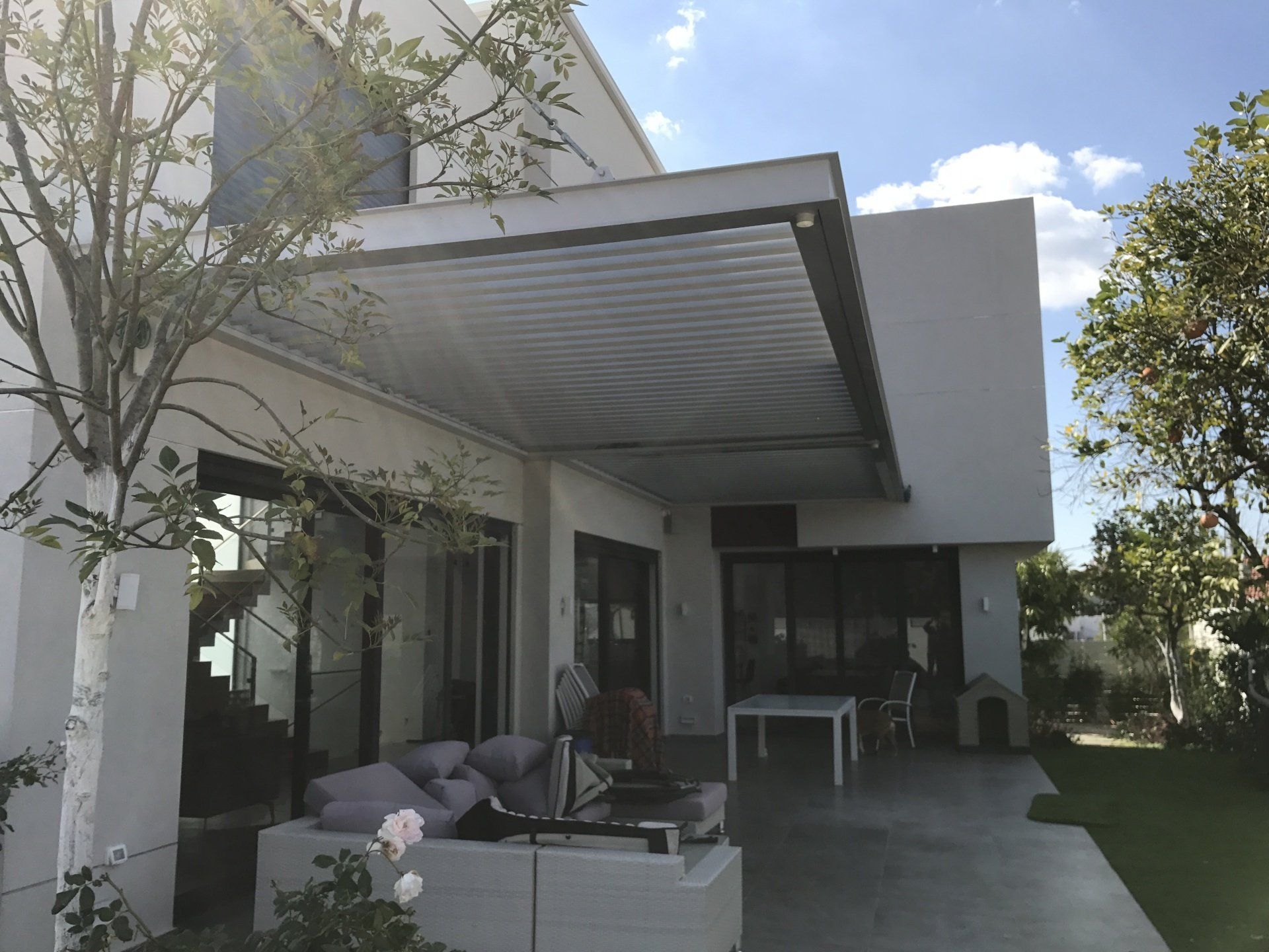 Modern house patio with covered seating, large windows, and a grassy yard under bright daylight
