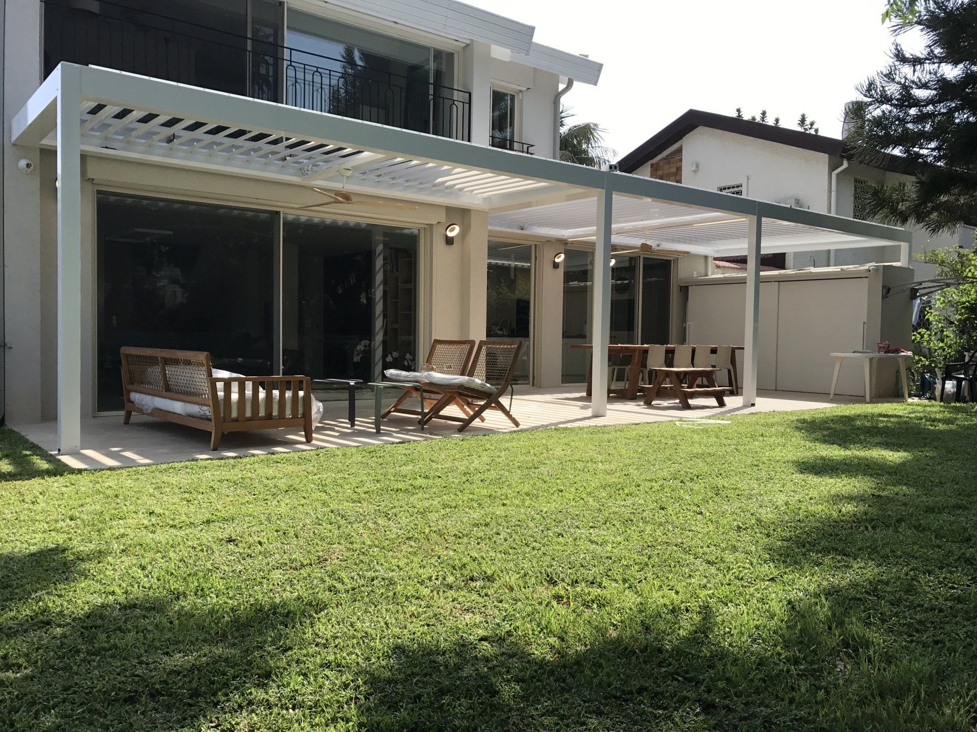 Modern house patio with outdoor seating, white pergola, and a green lawn in front