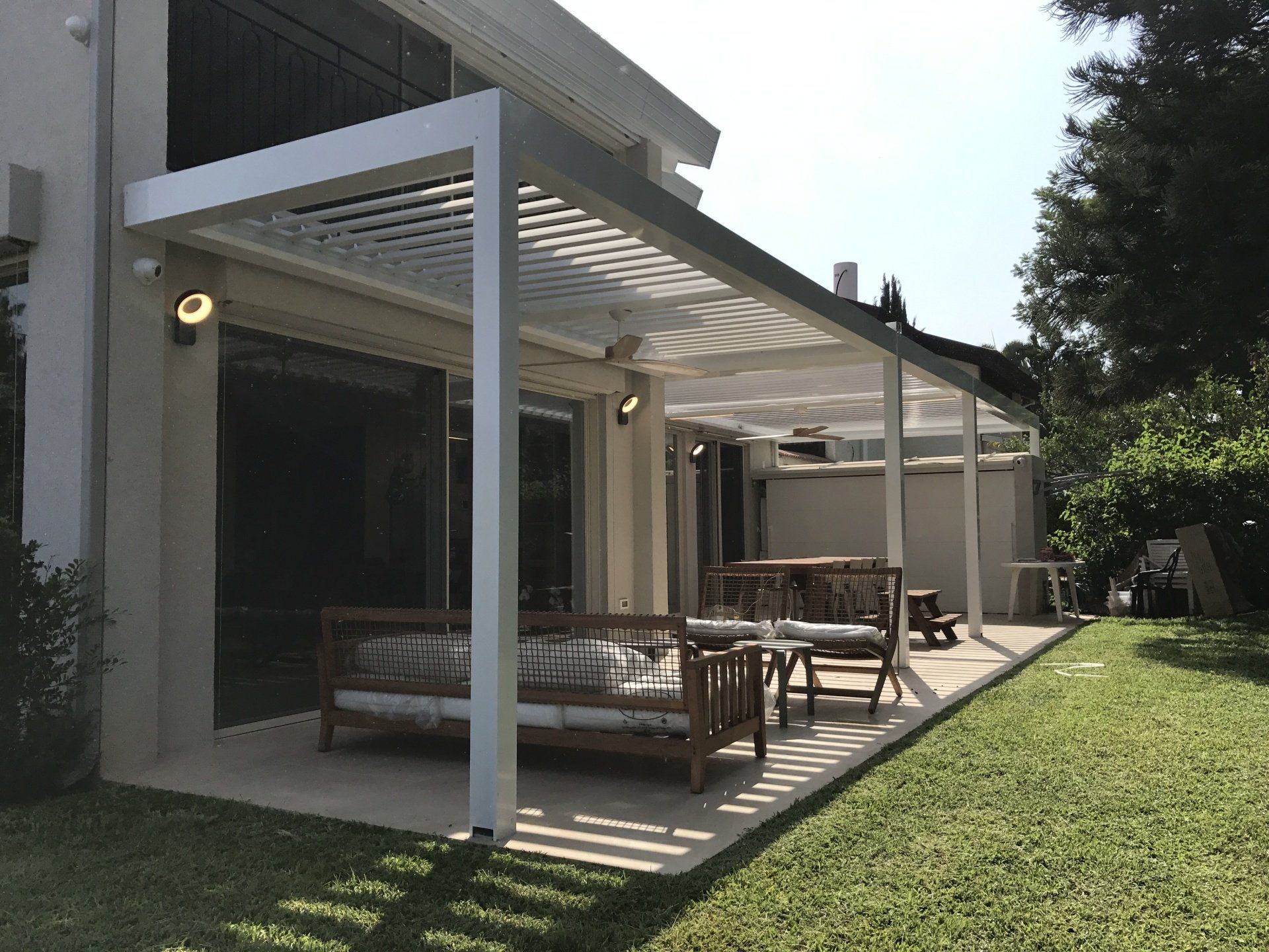 Covered patio with white pergola, outdoor seating, and a grassy yard beside a house