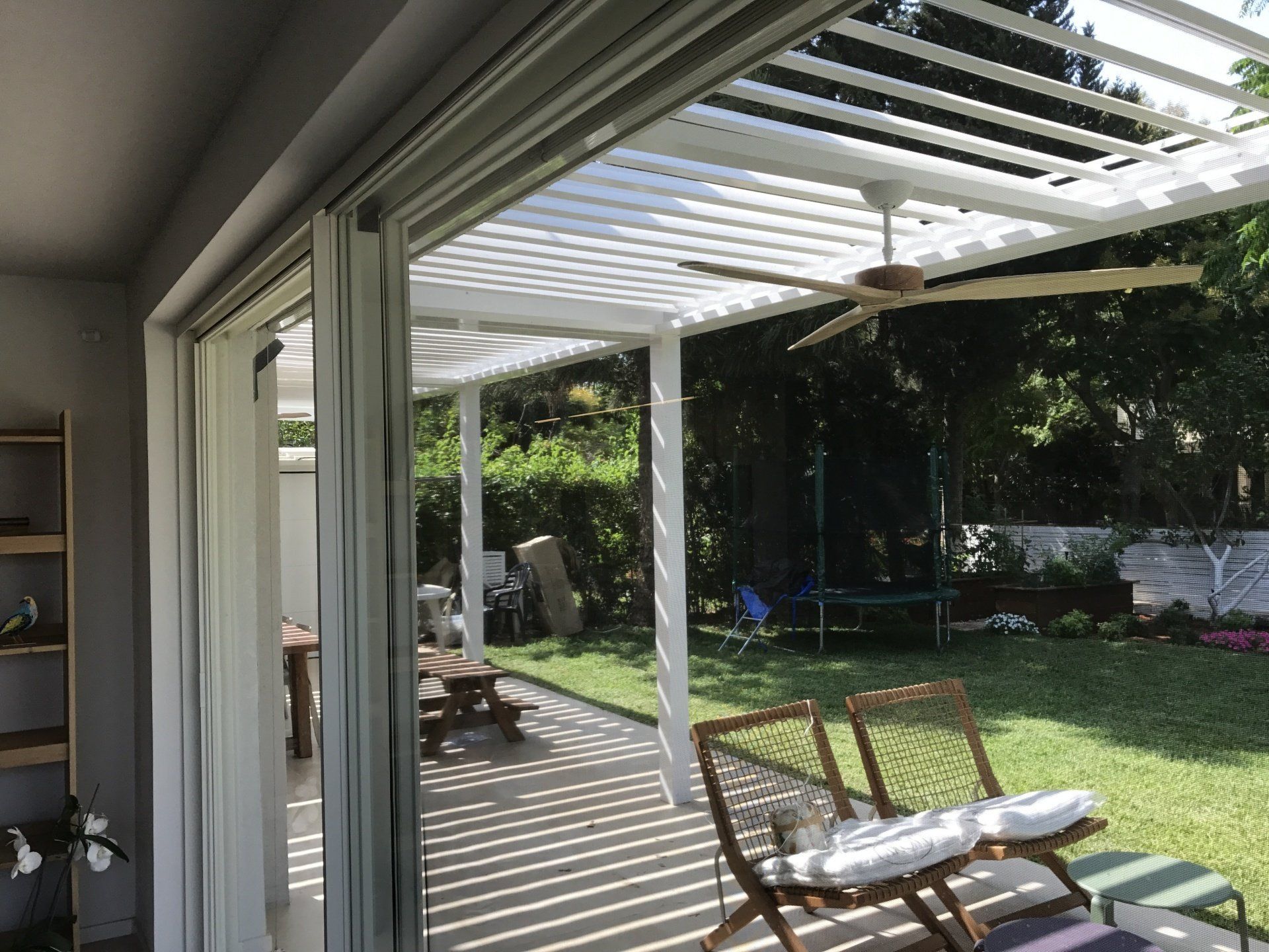 Patio view through sliding glass doors to a sunny backyard with pergola, lawn, and lounge chair