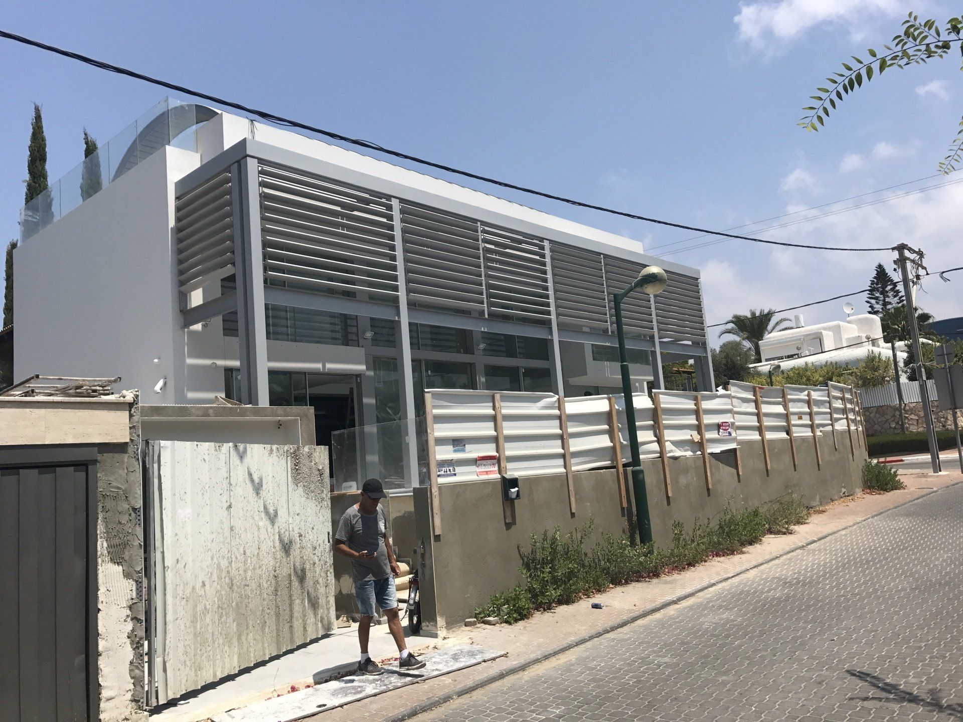 Modern white building behind a wall on a sunny street, with a person standing by the gate