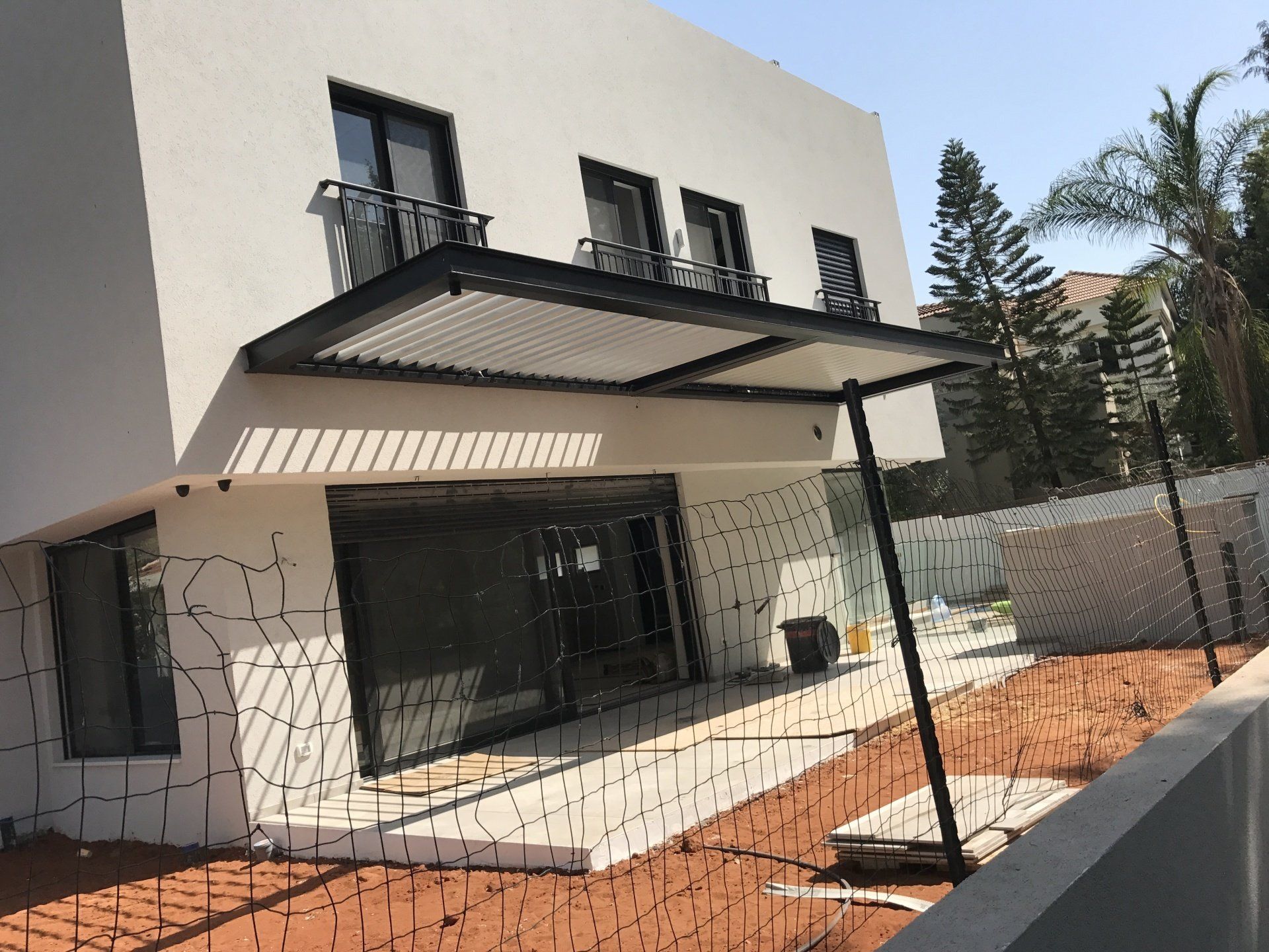 Modern white house exterior with a large black awning, balcony windows, and a fenced front yard.