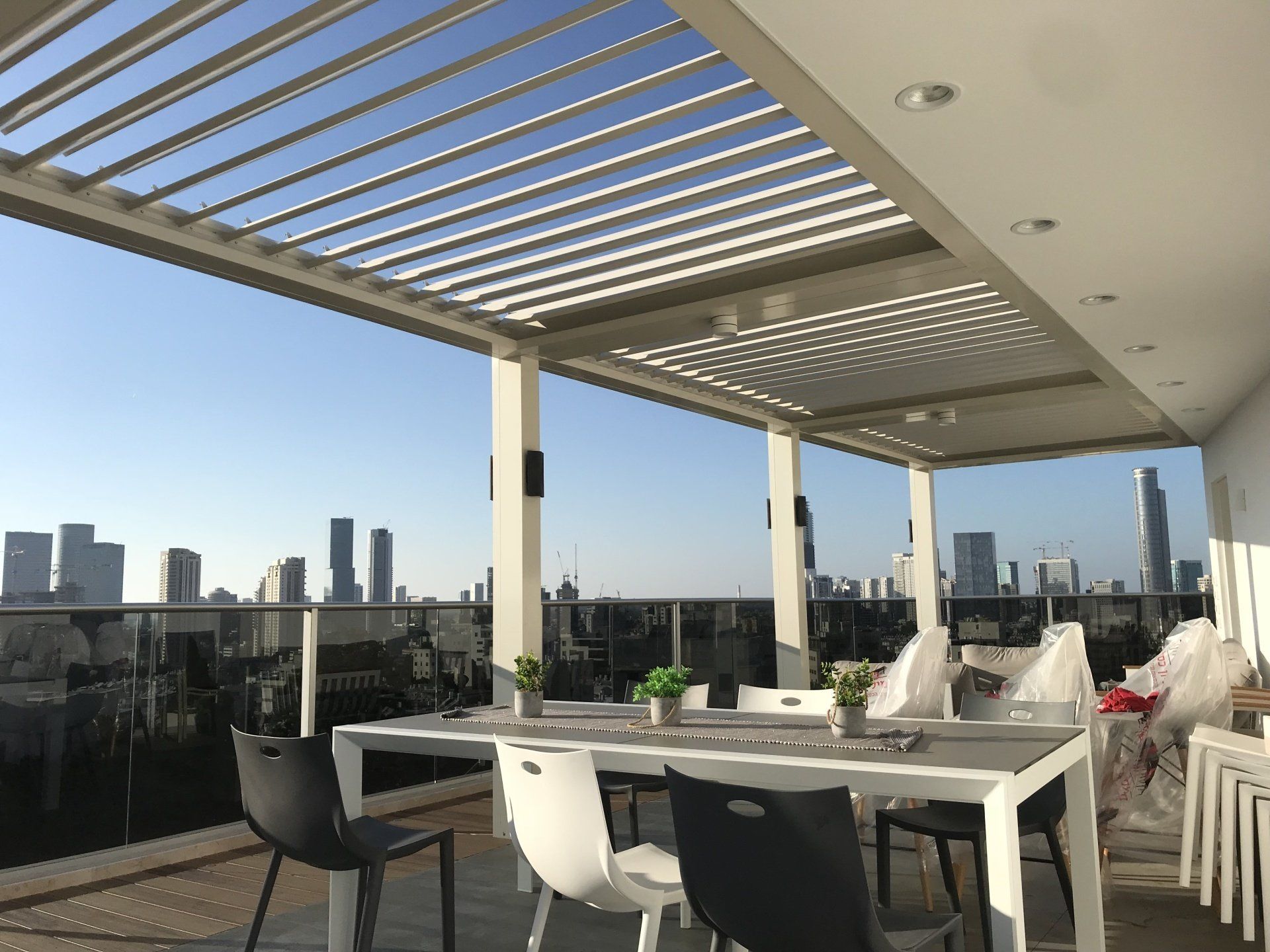 Rooftop patio with white table and chairs, pergola shade, and a city skyline in the distance