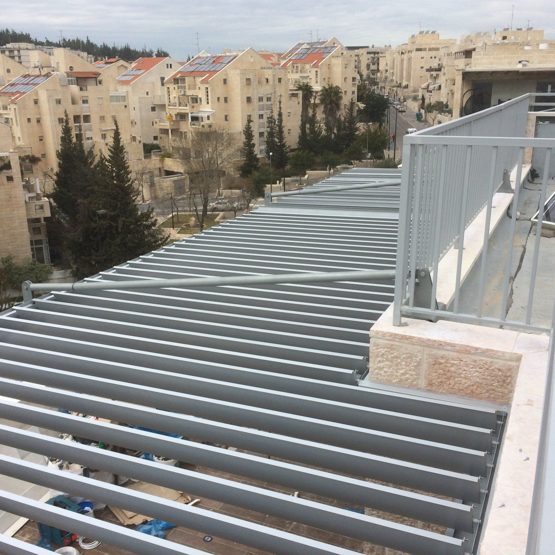 Rooftop with gray metal beams overlooking beige apartment buildings and trees