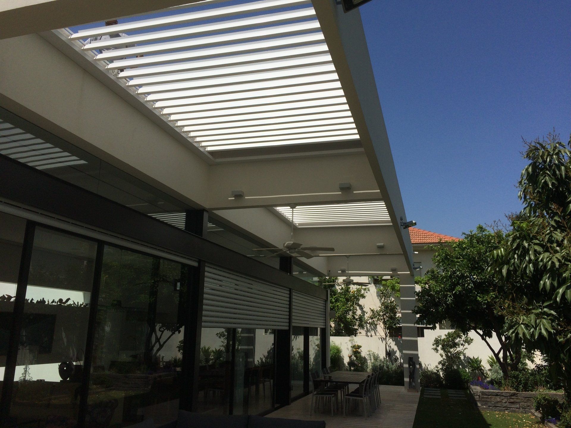 Patio with white pergola, glass doors, and trees under a clear blue sky