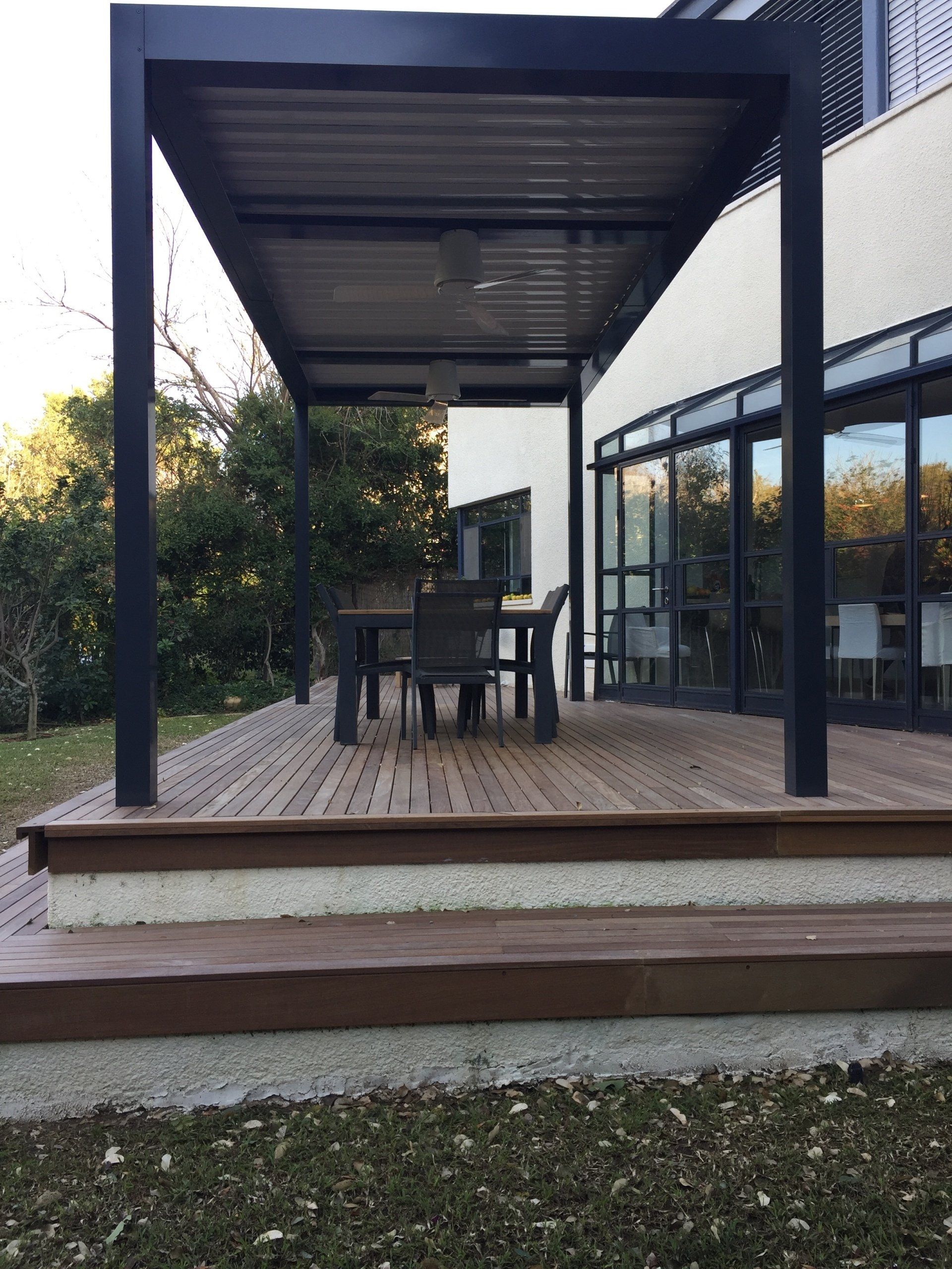 Modern patio with covered dining table, wooden deck, and glass sliding doors beside a garden.