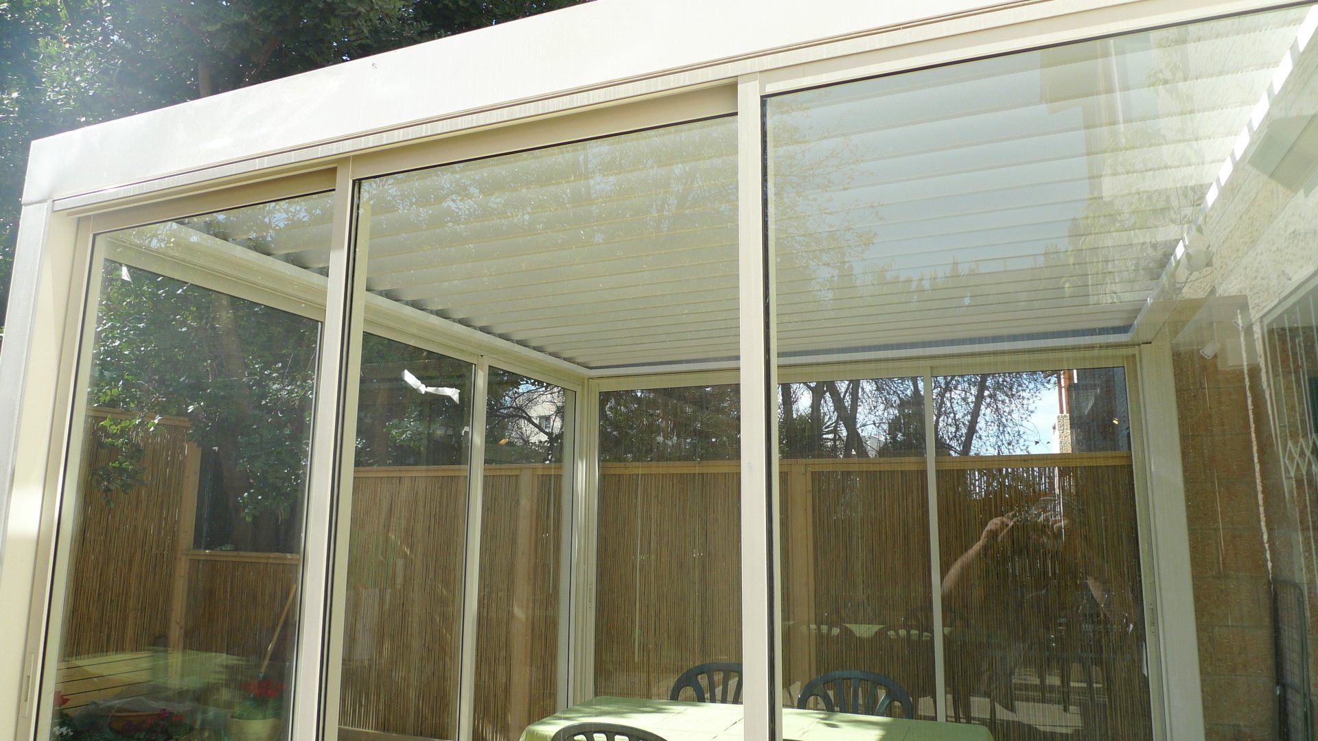 Sunroom with large glass windows and a white roof, overlooking a fenced backyard