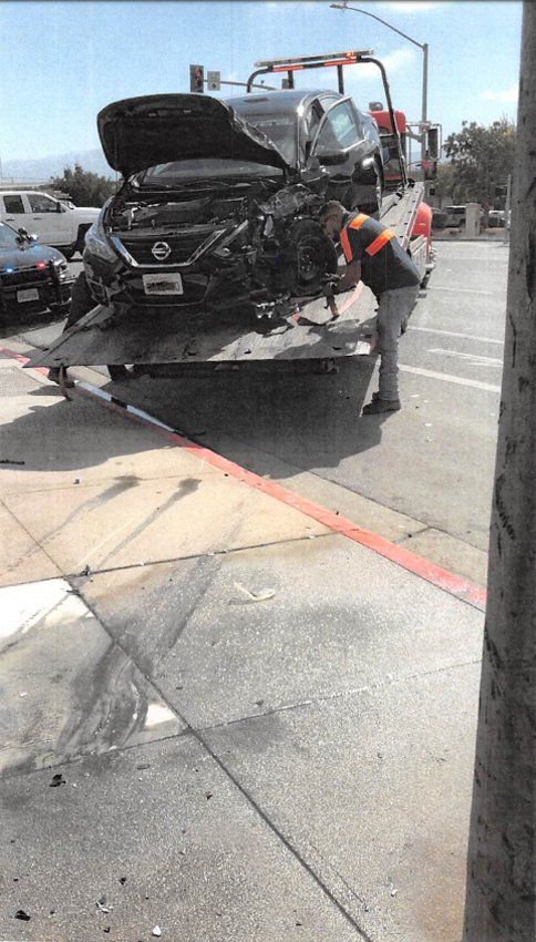A heavily damaged black car is loaded onto a tow truck after a collision on a street.