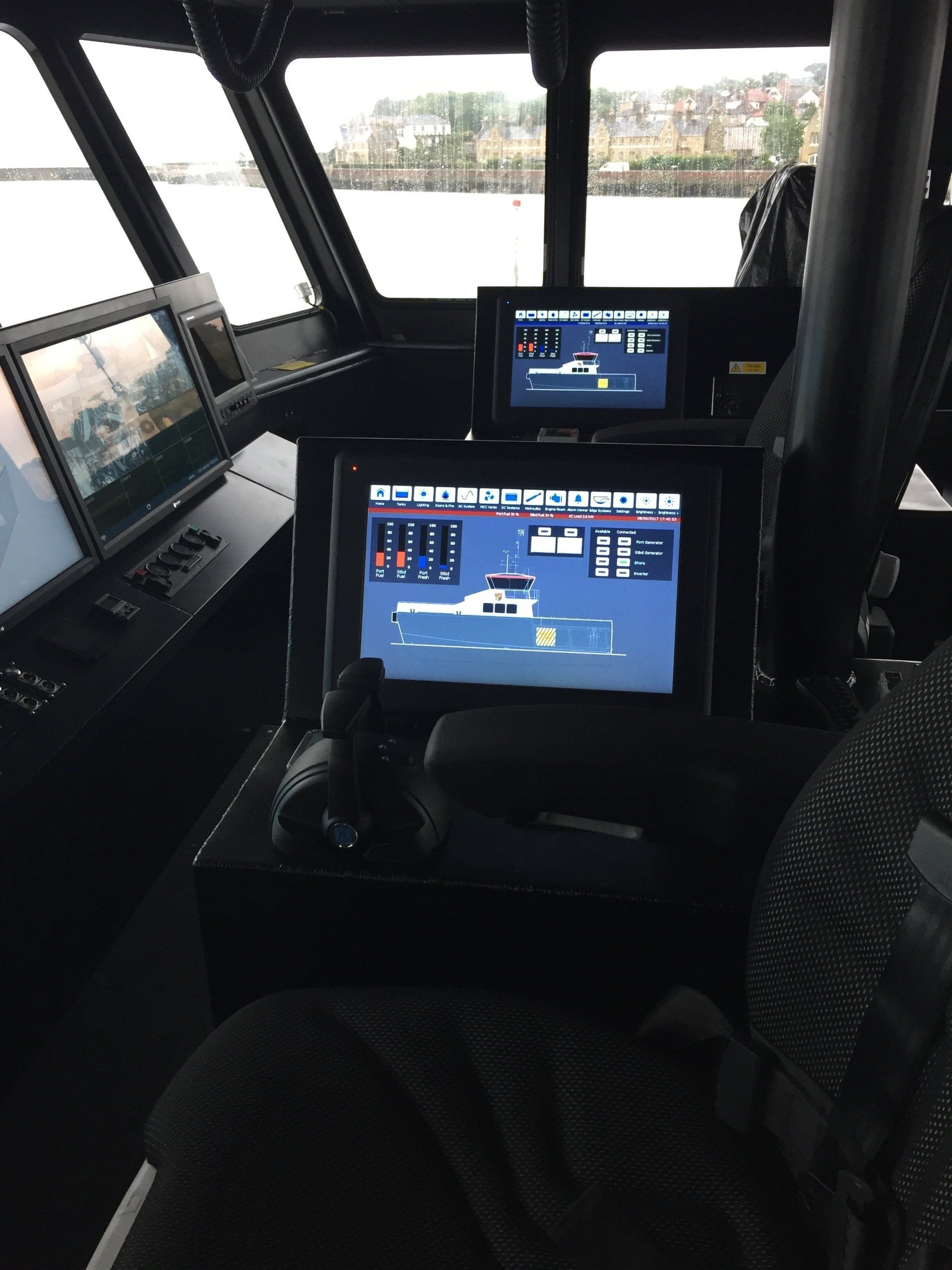 Inside a boat cabin, two navigation screens display charts and controls on the dashboard.