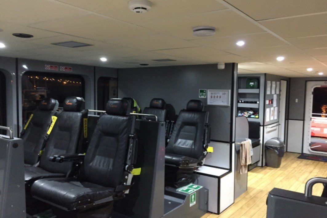 Interior of a modern transport cabin with black recliner seats, wood floor, and overhead lighting.