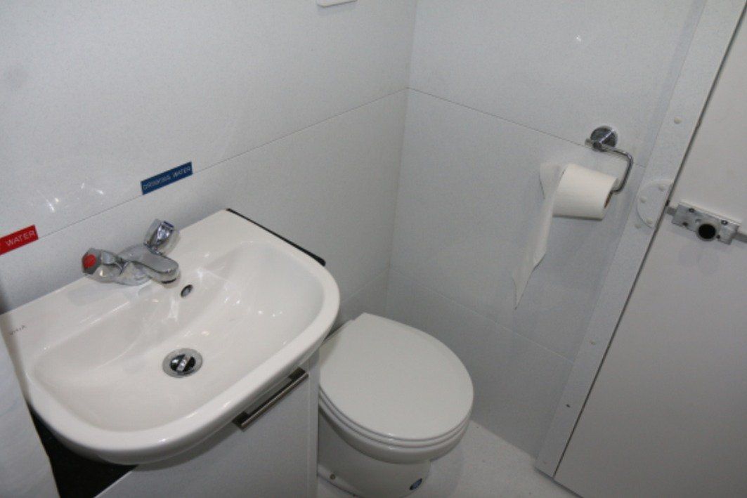 Small white bathroom with sink, toilet, and toilet paper holder against tiled walls.