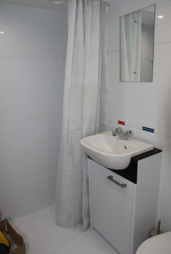 Small white bathroom sink with mirror, shower curtain, and tiled walls.