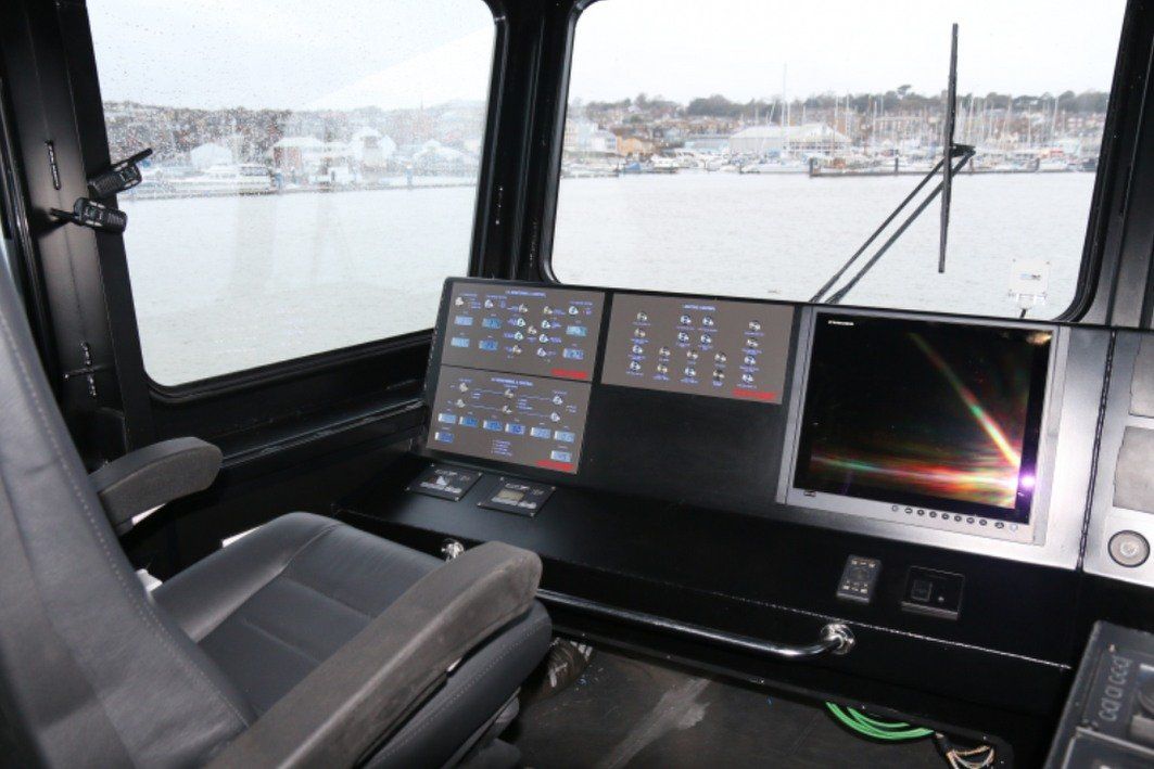 Boats’ helm with dashboard screens and chairs, overlooking a harbor through large windows.