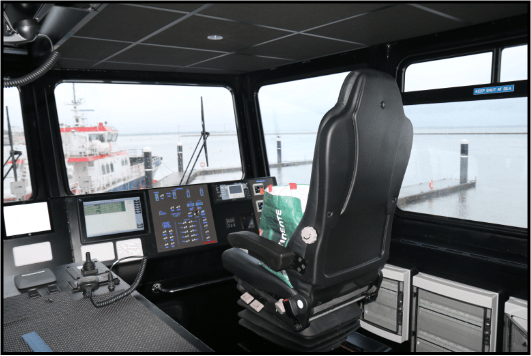 Inside a boat pilothouse, with steering chair, controls, and foggy water visible through large windows.