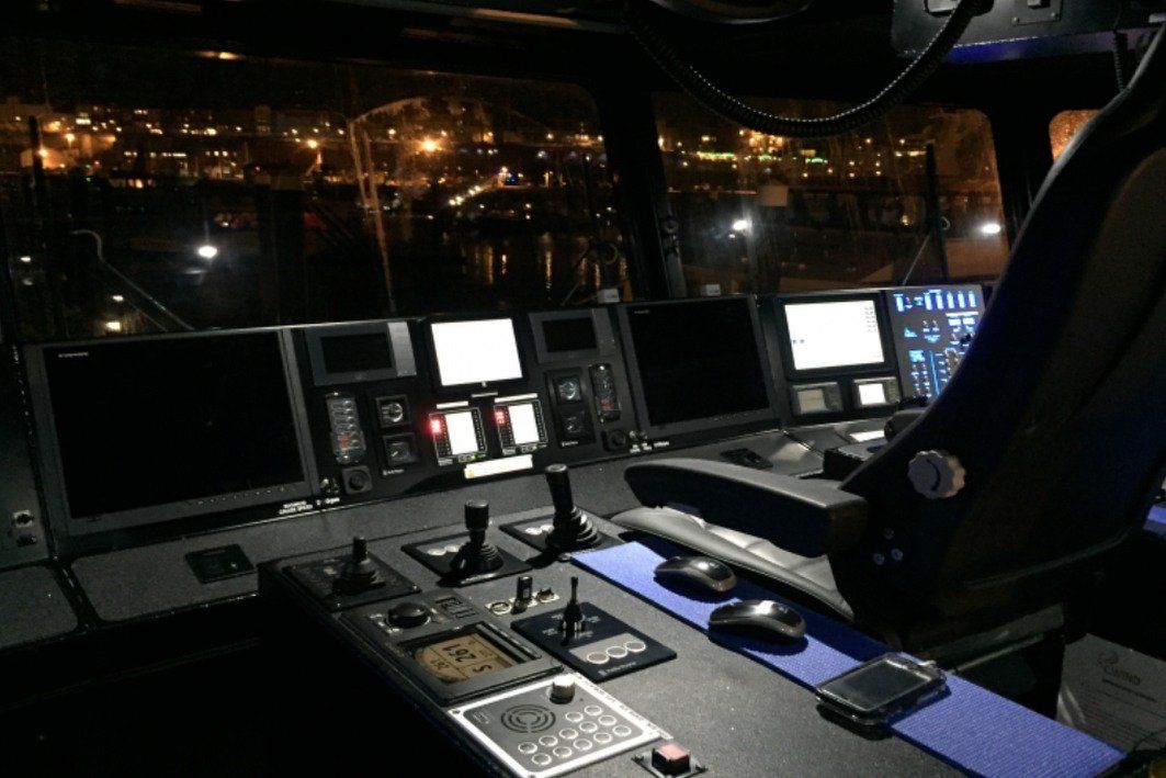 Cockpit control station at night with illuminated monitors and city lights outside the windows