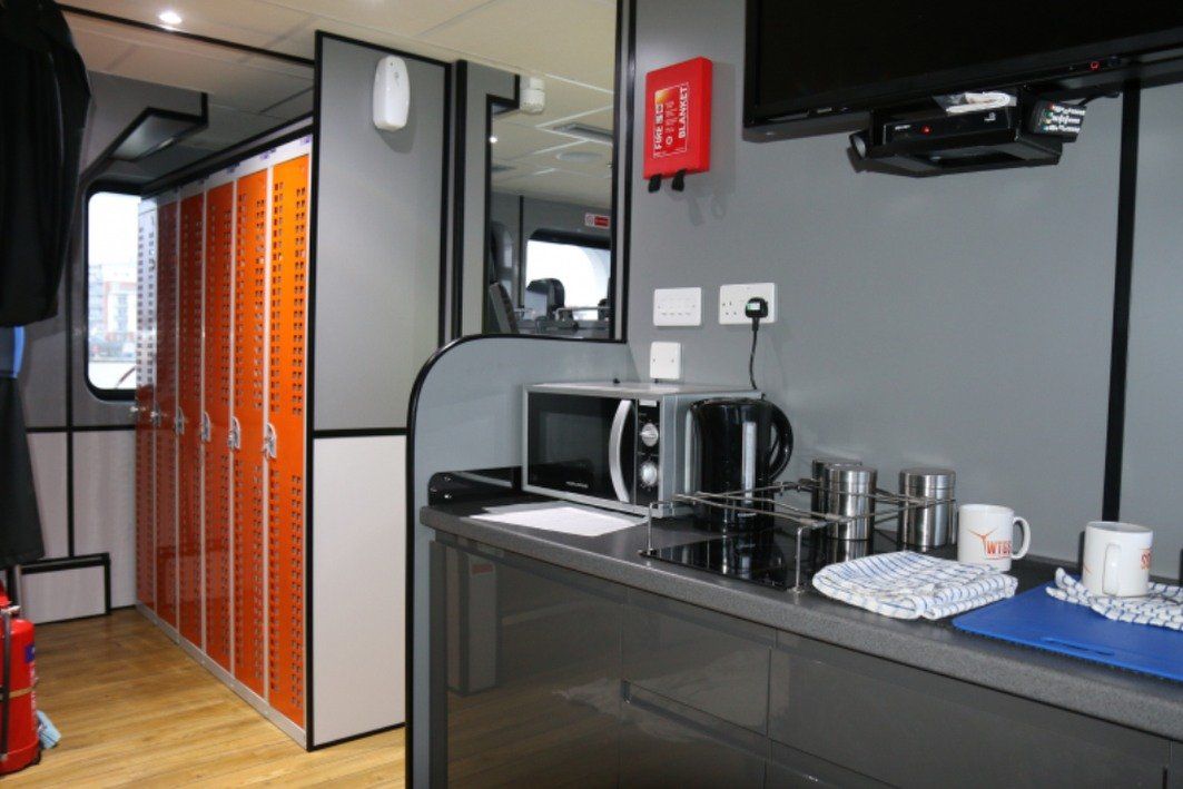 Compact kitchenette with sink, microwave, cups, and orange storage lockers in a small room