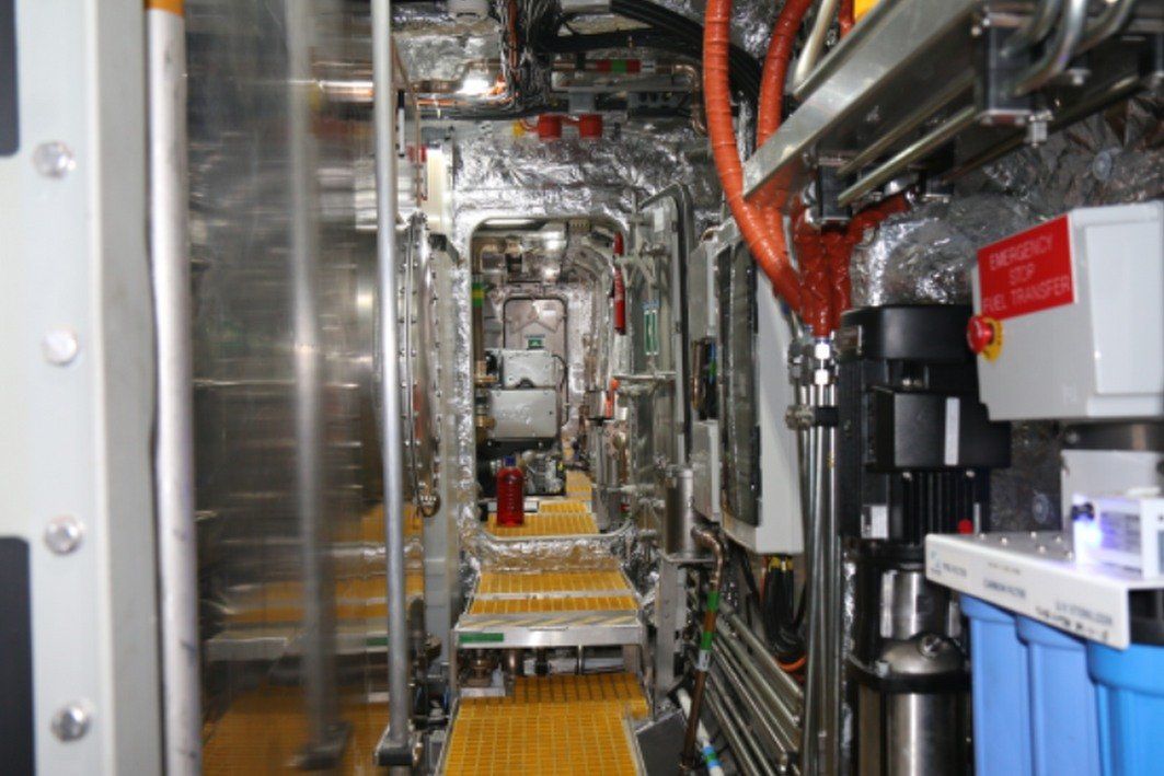 Industrial equipment corridor with pipes, cables, and machinery in a narrow metal-lined space