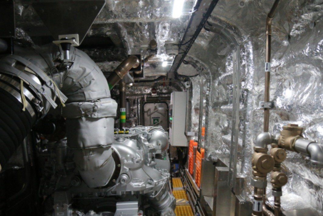 Industrial machinery and insulated pipes in a narrow metallic engine room corridor