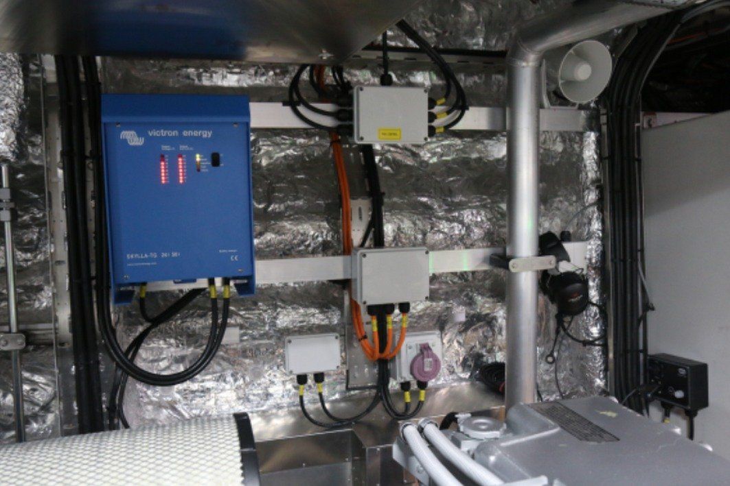 Utility room with blue control panel, pipes, wiring, and insulated ductwork.