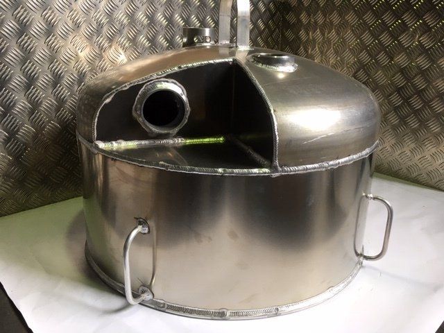 Stainless steel industrial tank with domed lid and pipe opening, set against a metal wall.