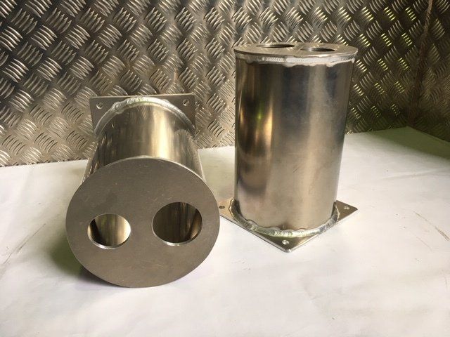 Two shiny metal cylindrical parts on a white surface, one lying down with two round holes in its end.