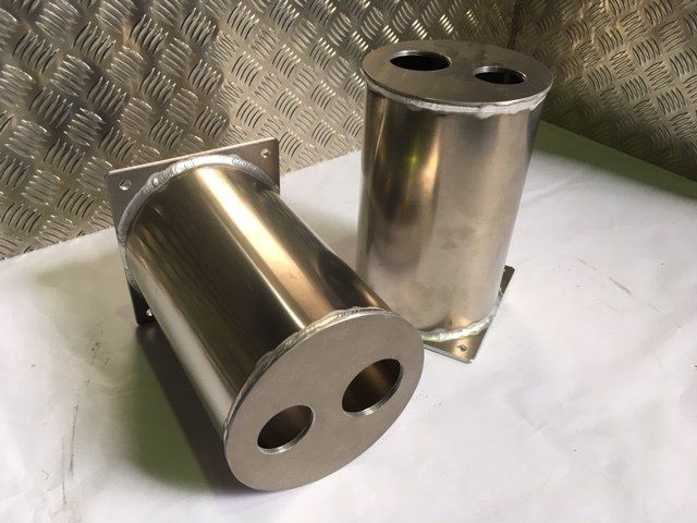 Two polished metal cylindrical parts on a white surface, one lying down and one standing upright.