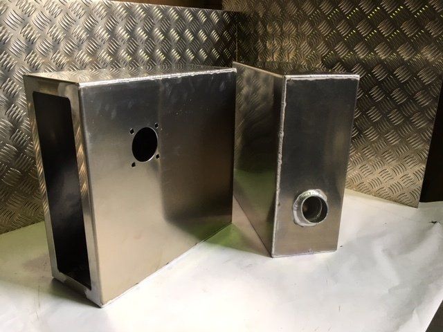 Two stainless steel rectangular metal boxes with circular holes, shown on a textured metal surface.