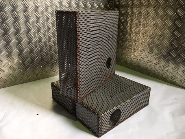 Perforated metal L-shaped enclosure with round holes, set on a white surface against a diamond-plate metal background