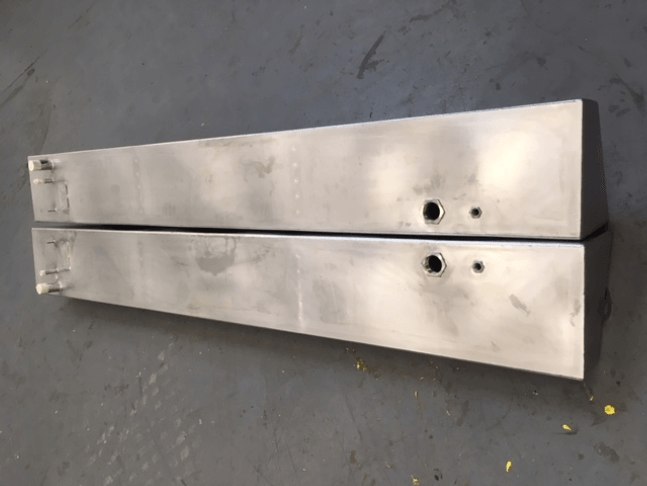Two long silver metal panels lying on a gray floor, each with two round holes near one end.
