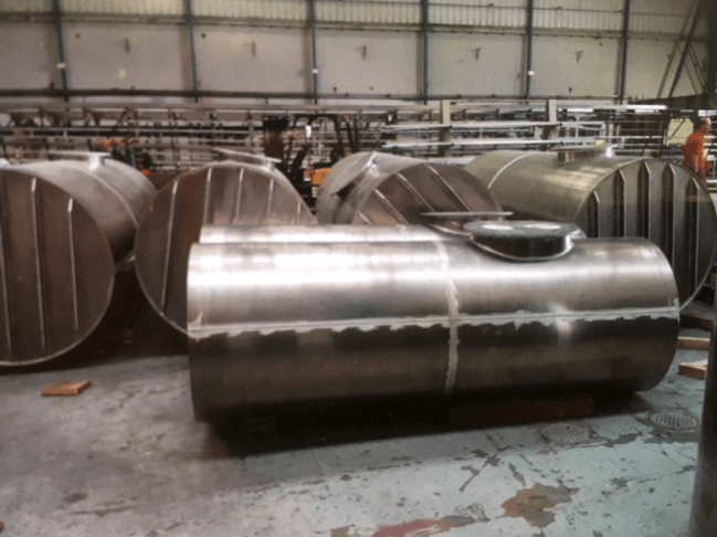 Large stainless steel cylindrical tank in an industrial workshop, with other metal tanks in the background