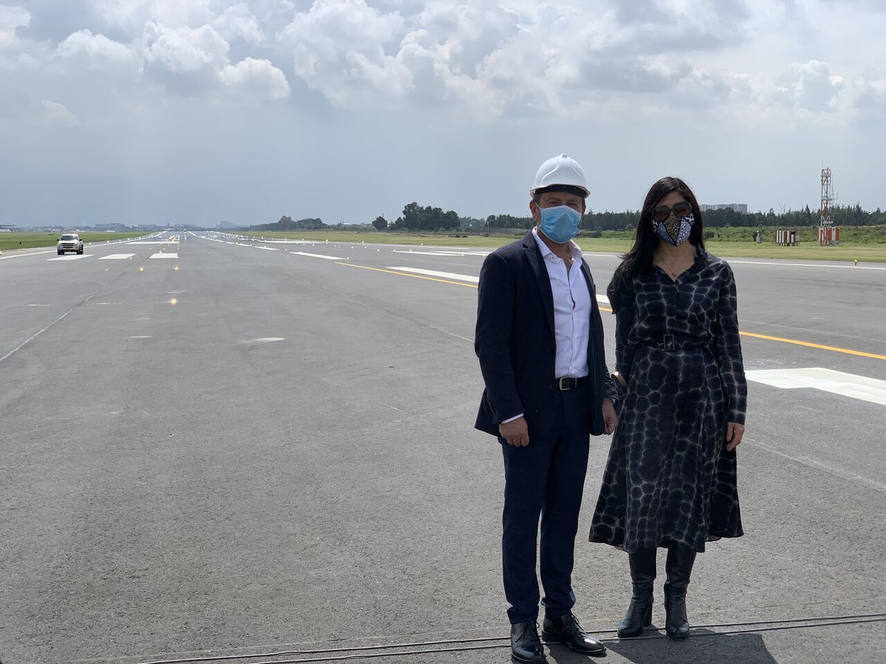 Un hombre y una mujer con máscaras están parados en la pista de un aeropuerto.