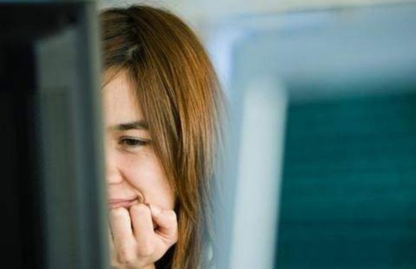 Una mujer se muerde las uñas mientras mira la pantalla de una computadora.