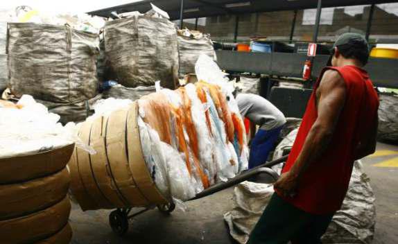 Un hombre con una camiseta roja empuja un carrito lleno de bolsas de plástico.