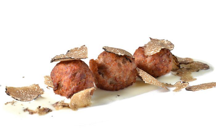 Tre polpette con tartufo sopra, su una superficie bianca.