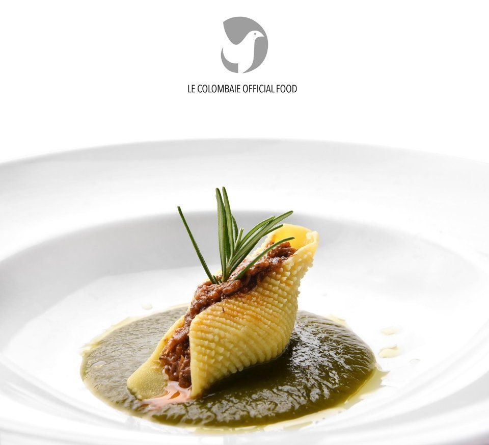 Un piatto bianco sormontato da una conchiglia ripiena di carne e salsa