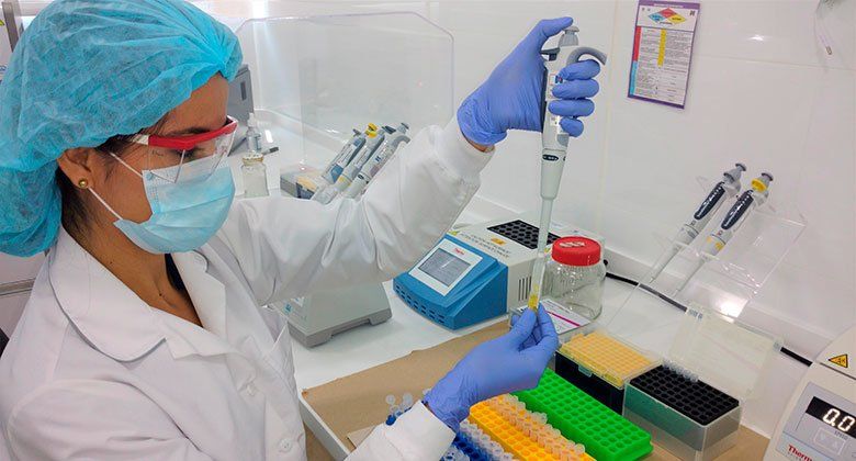 Una mujer con bata de laboratorio y mascarilla utiliza una pipeta.