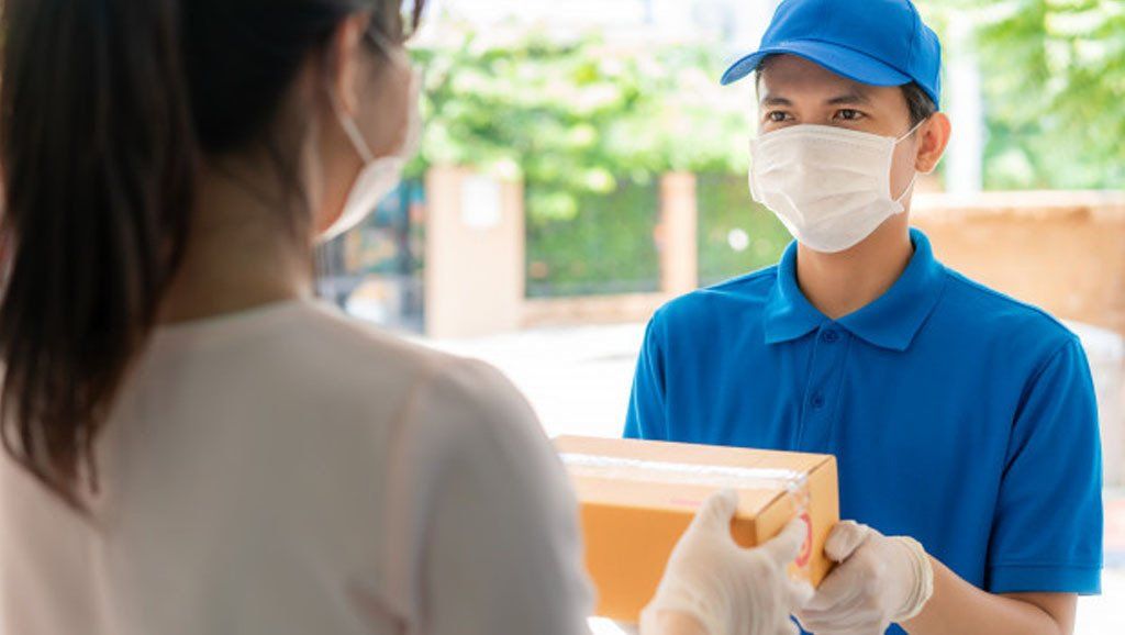 Un repartidor con mascarilla y guantes entrega un paquete a una mujer.