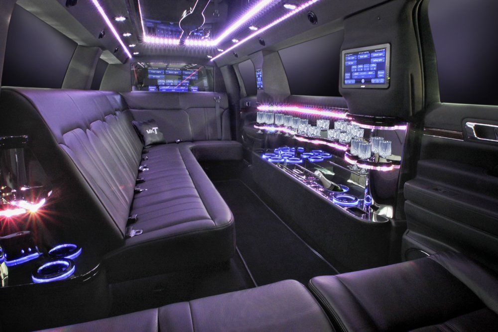 Inside of a black limousine with purple lighting and leather seats.