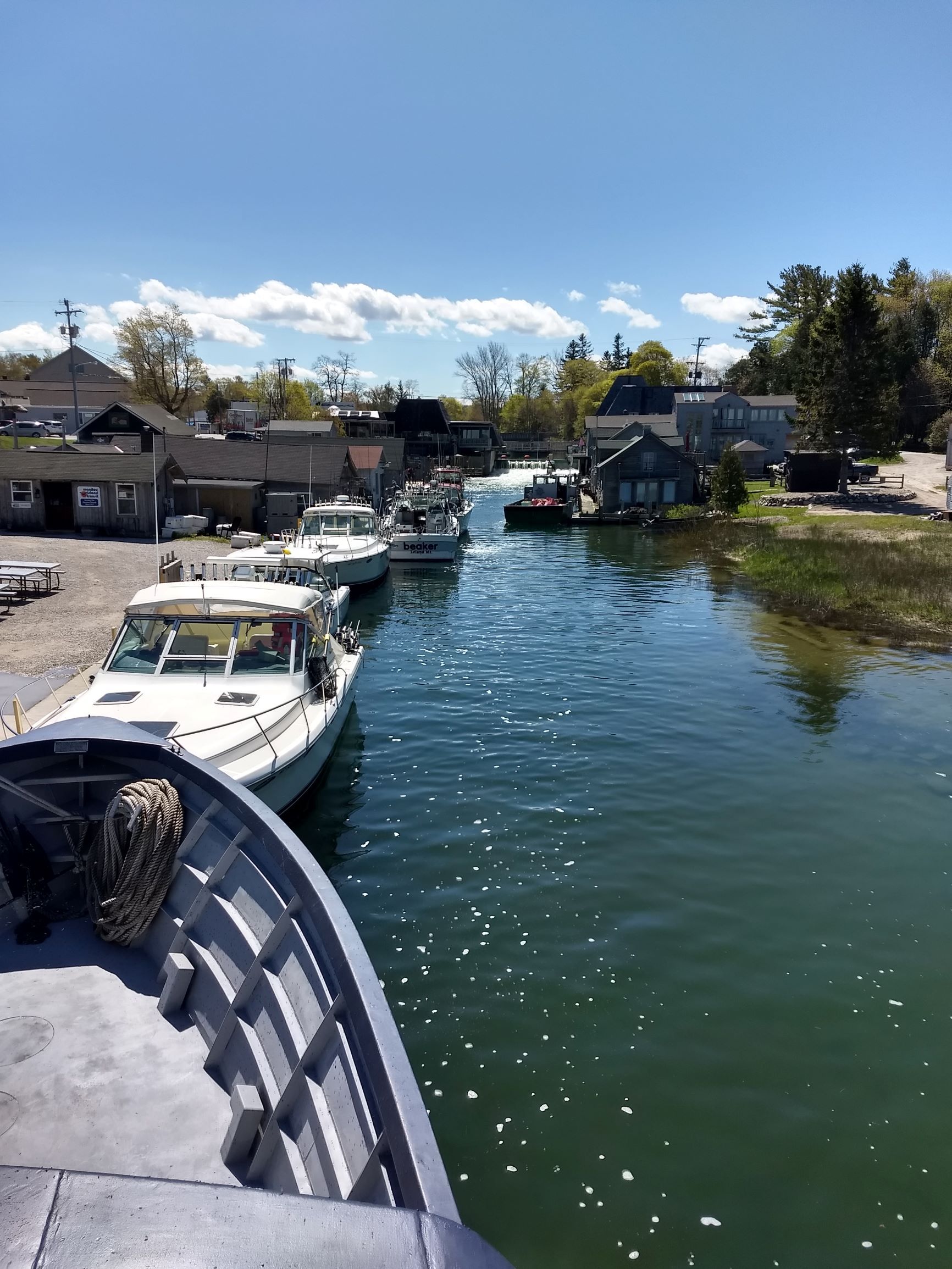 Narrow canal with moored boats, houses on both sides, and a sunny blue sky