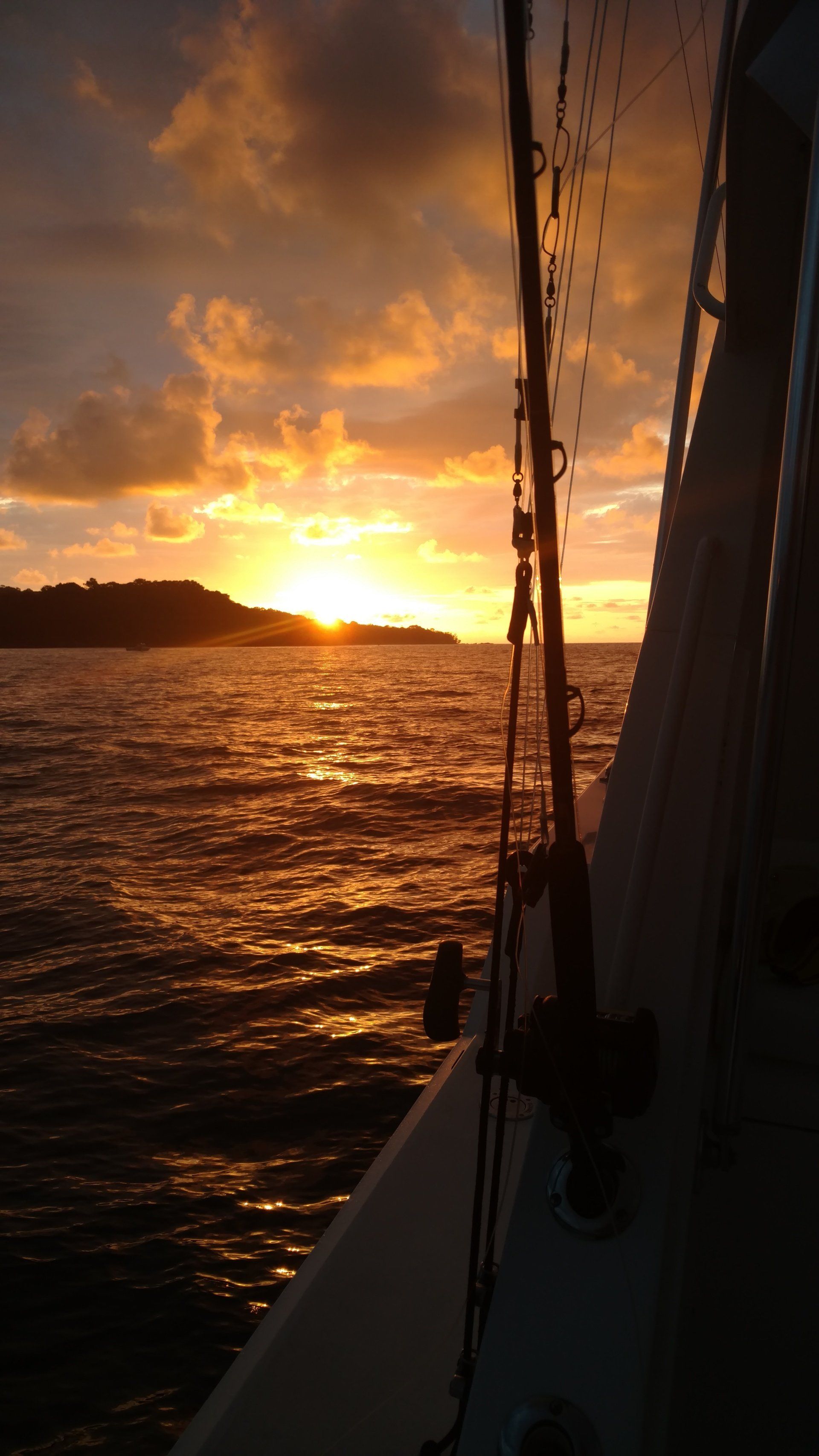 Sunset over choppy water, viewed from a sailboat with rigging in silhouette