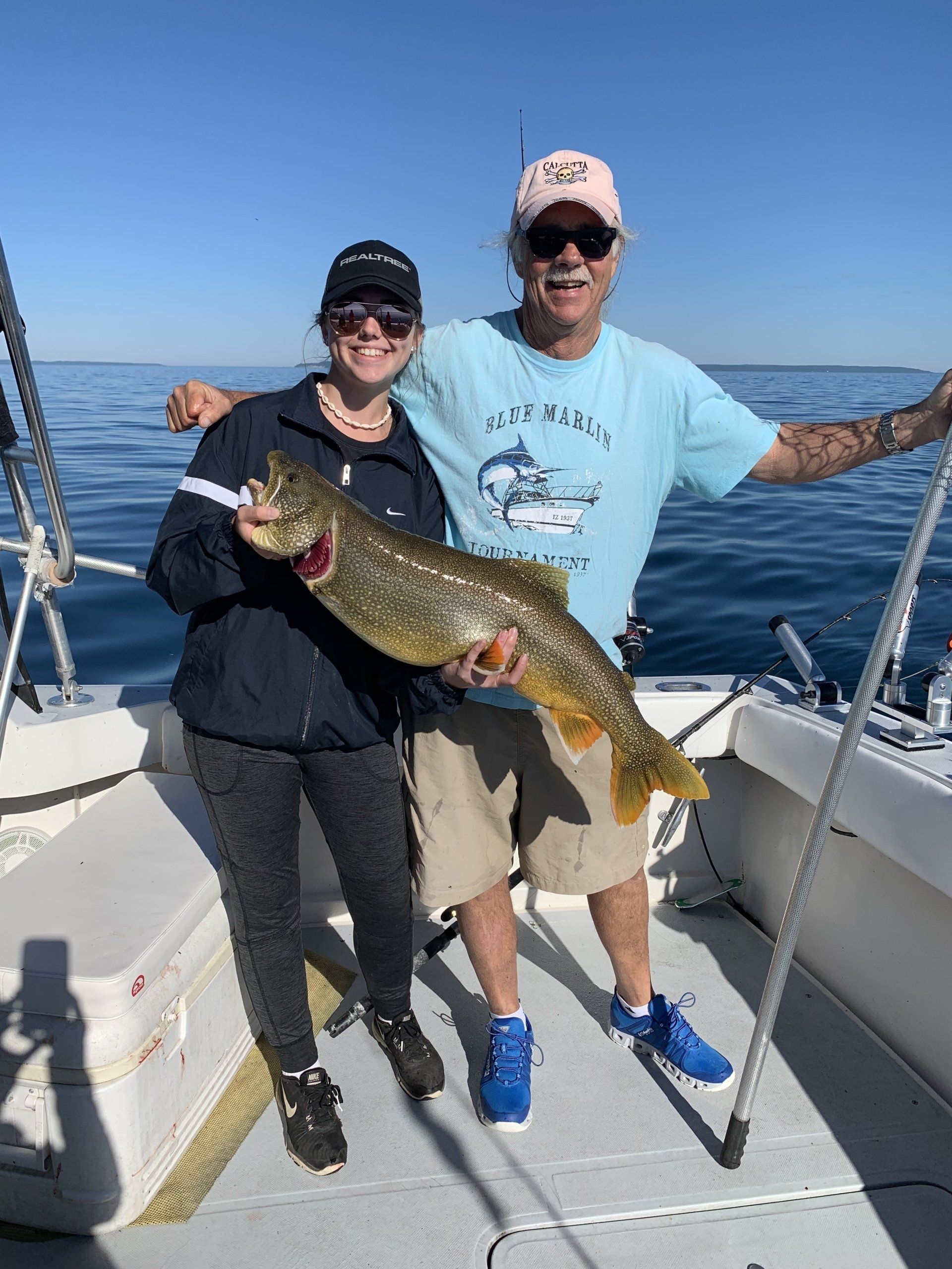 Two people on a boat holding a large fish on a sunny day at sea