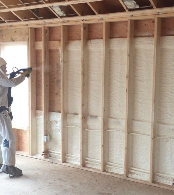 Man spraying insulation foam into the wall of a room under construction.