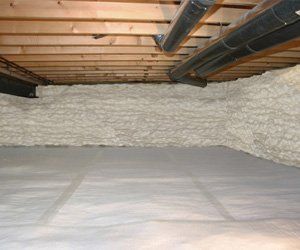 Crawl space insulated with spray foam on walls and a white vapor barrier on the ground. Wooden beams overhead.