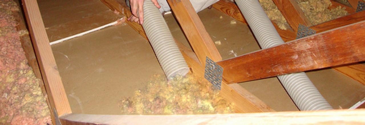 Interior view of an attic with insulation and air ducts installed between wooden beams.