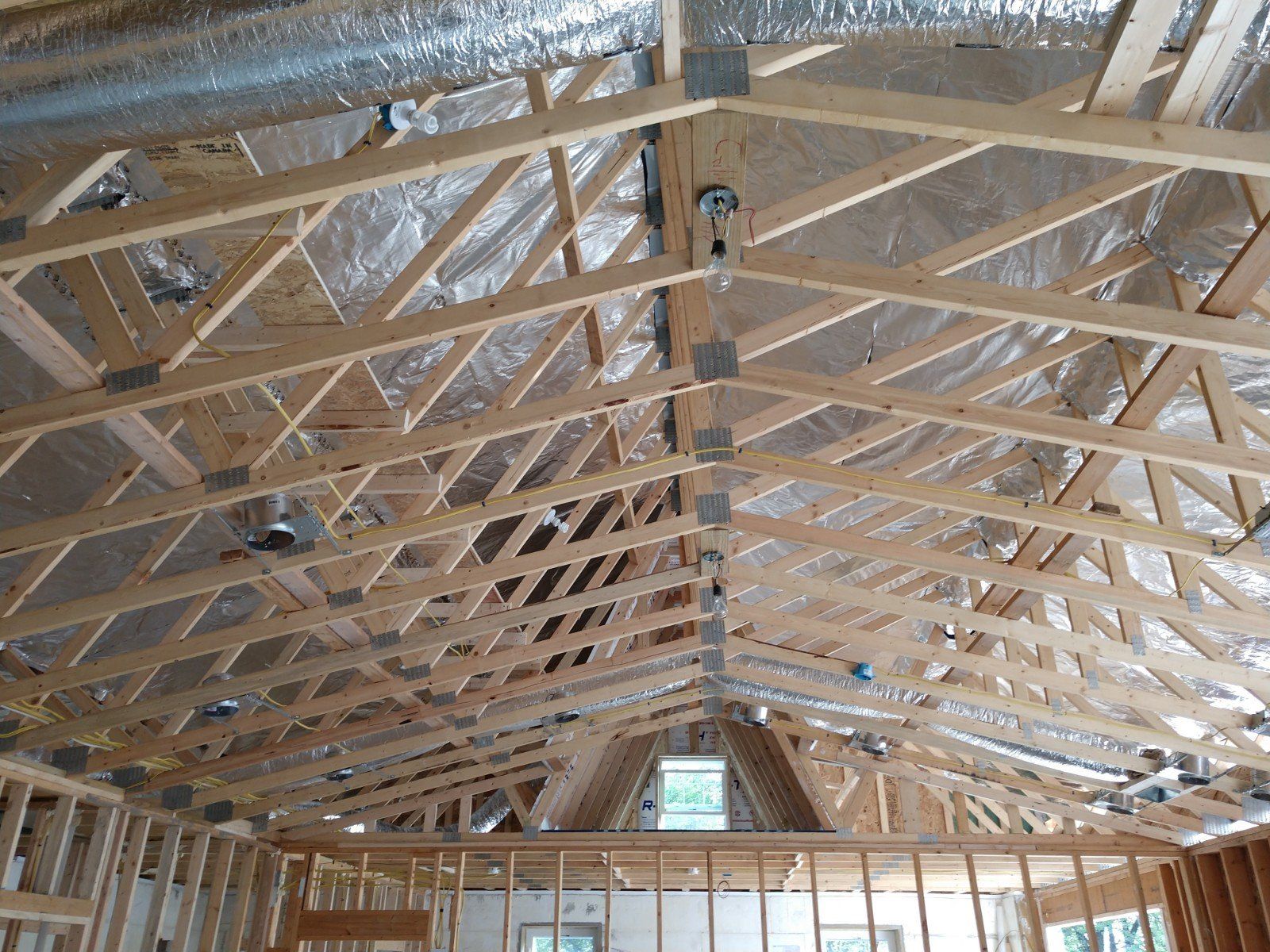 Interior view of a building under construction, showing wooden roof trusses and silver insulation.