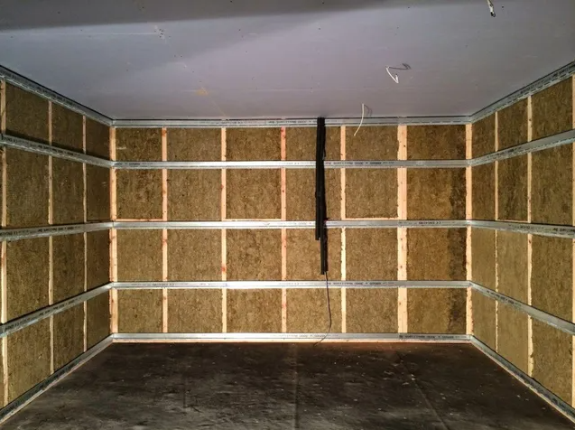 Interior of a room with insulated walls made of brown panels and metal framing.